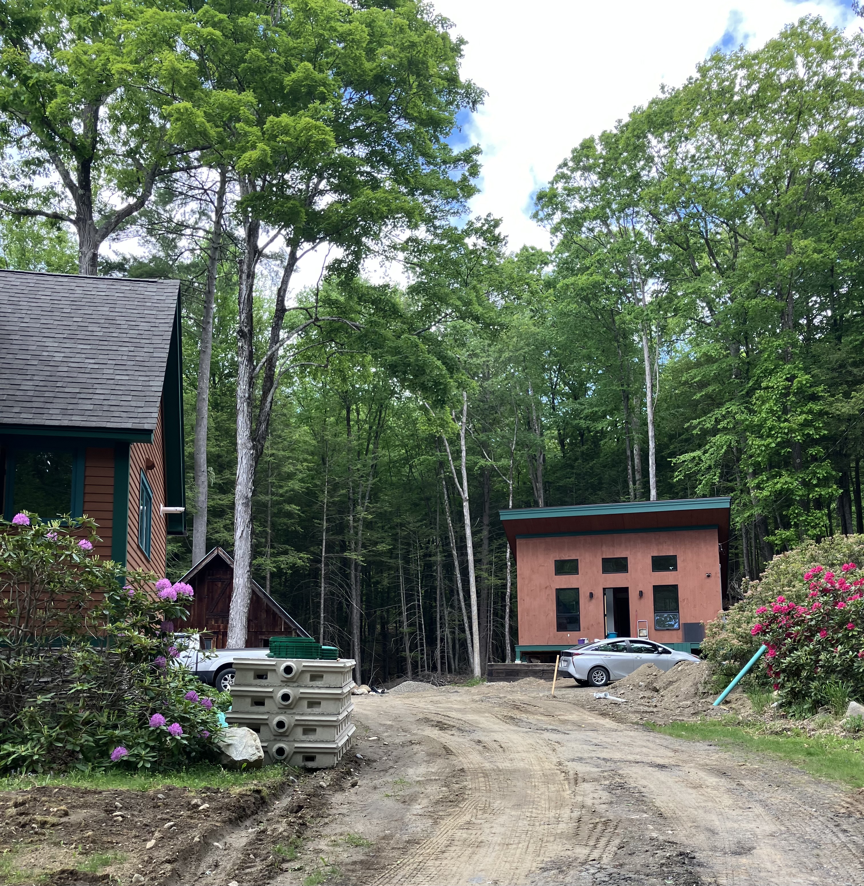 Wide view of a standalone backyard ADU in Shelburne, Massachusetts showing a completed exterior beside the main home in a wooded setting